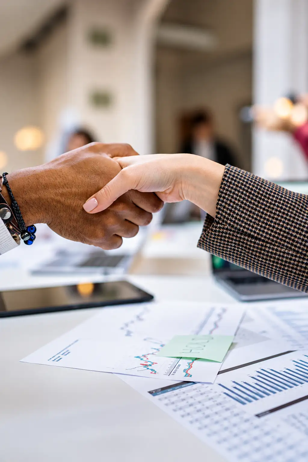 A handshake across a desk covered in financial charts
